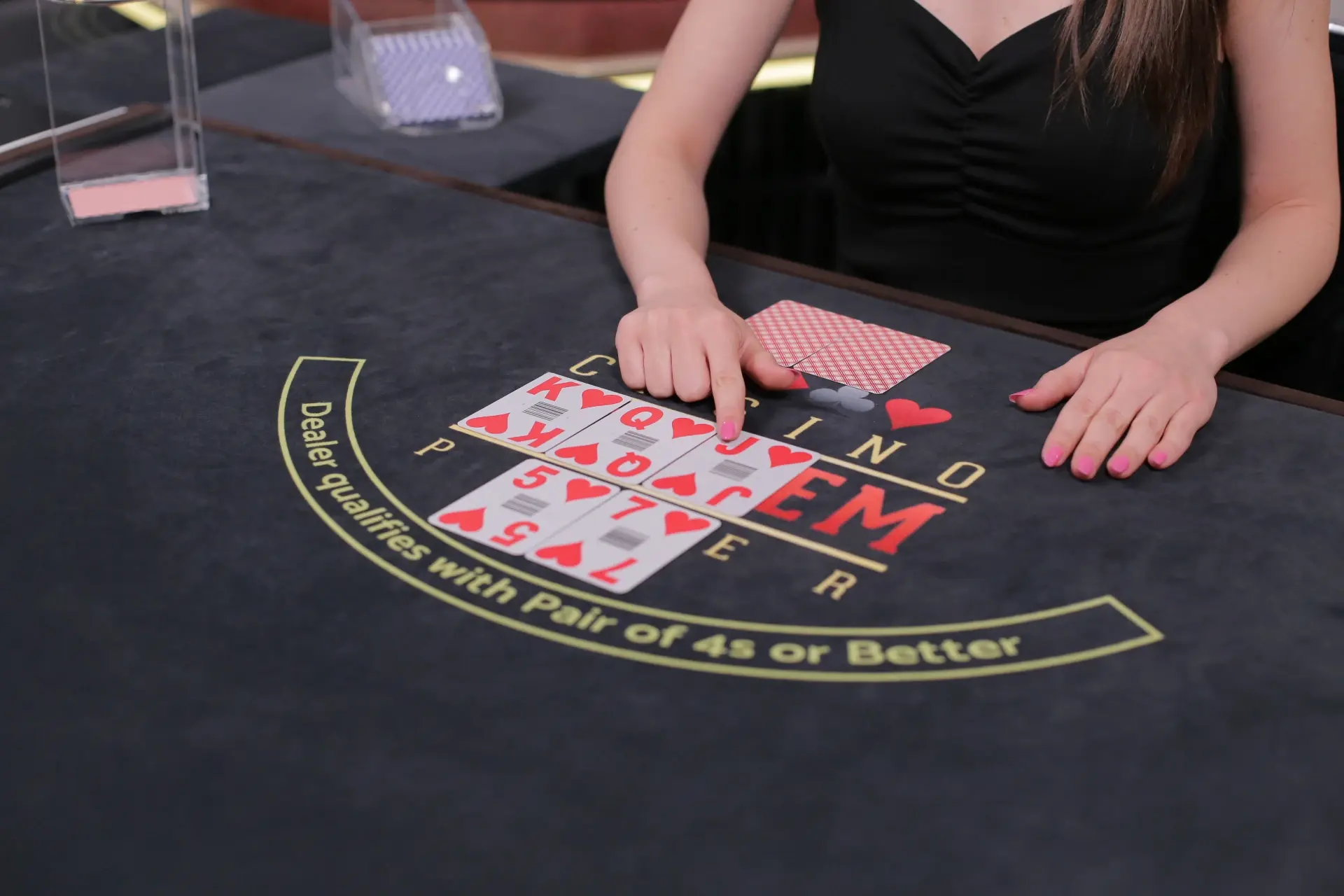 Výherní kombinace v Casino Hold’em – krupiérka předvádí karty na stole Krupiérka ukazuje výherní kombinaci karet na stole během hry Casino Hold’em